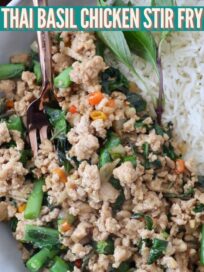 thai basil chicken in bowl with fresh Thai basil leaves, cooked rice and fork