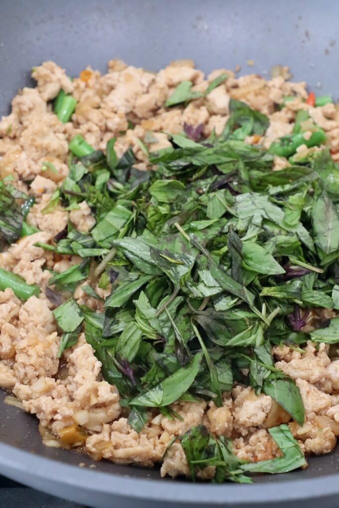 fresh Thai basil in large pan with cooked ground chicken