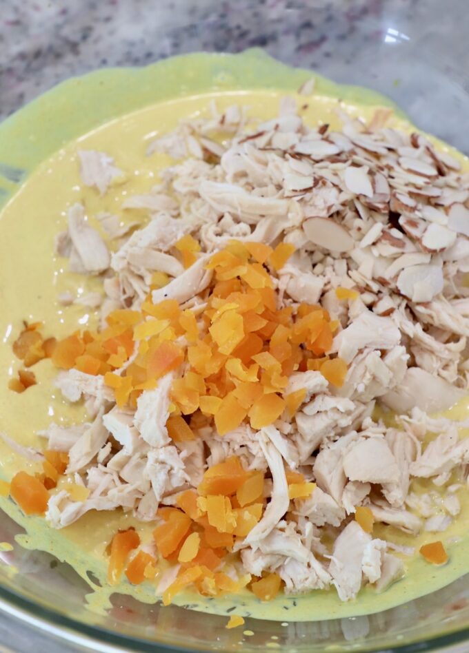 cooked, shredded chicken in large glass bowl with creamy curry sauce and diced dried apricots