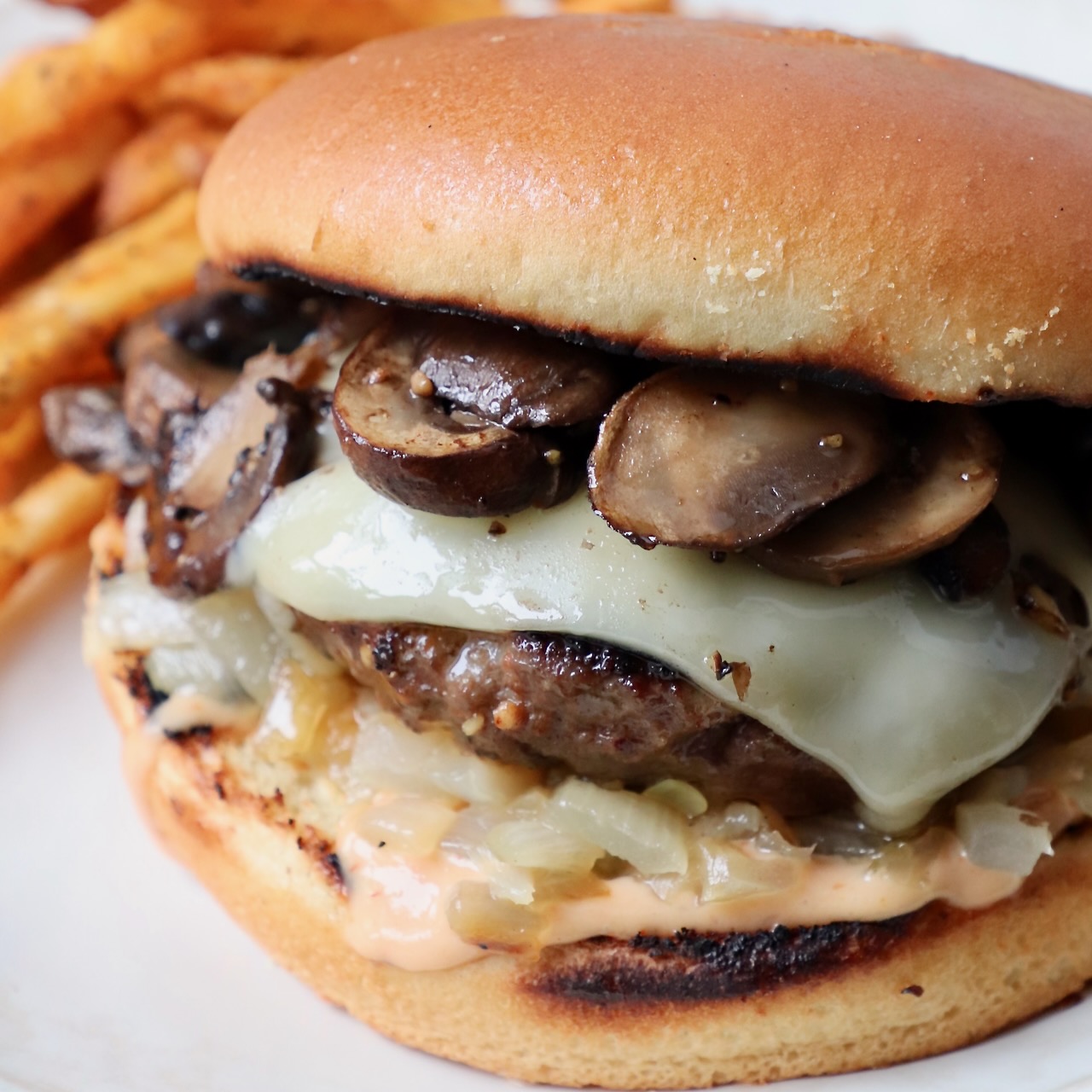 prepared mushroom swiss burger on plate with fries