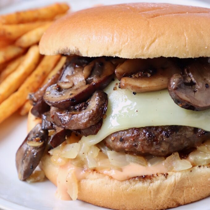 cooked cheeseburger topped with sauteed mushrooms on plate with seasoned fries