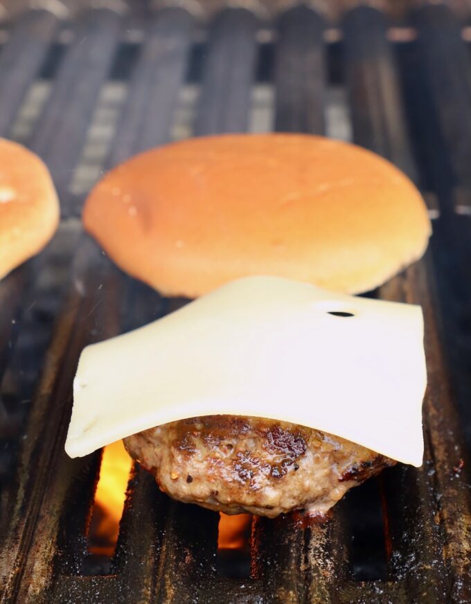 hamburger patty topped with swiss cheese on a grill next to hamburger buns