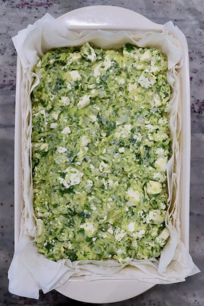 sheets of phyllo dough in baking dish covered with zucchini feta filling