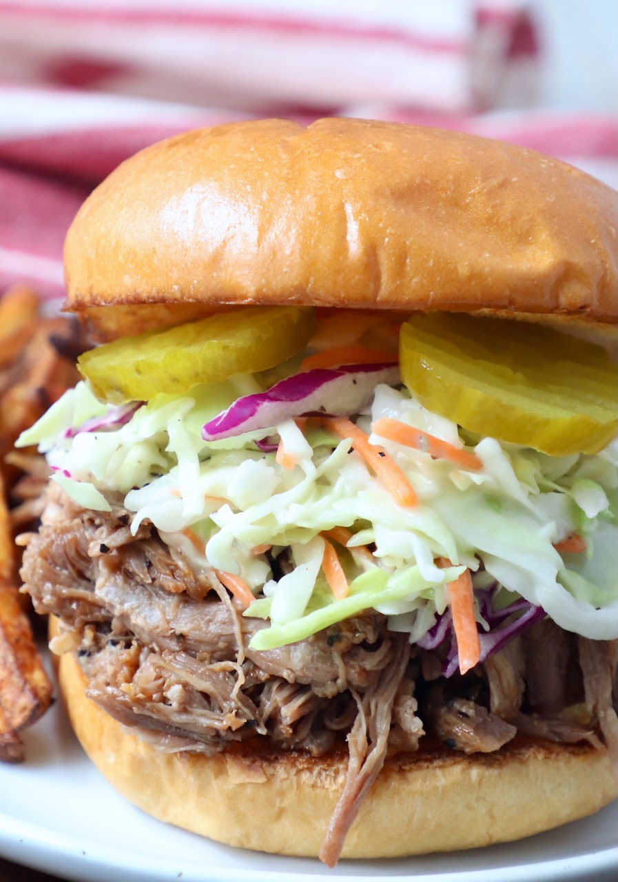 pulled pork sandwich topped with coleslaw and pickles on plate