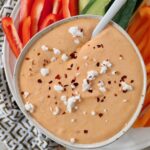 roasted red pepper feta dip in bowl topped with feta cheese crumbles and red pepper flakes