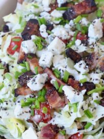 chopped salad in bowl topped with chopped bacon and blue cheese crumbles