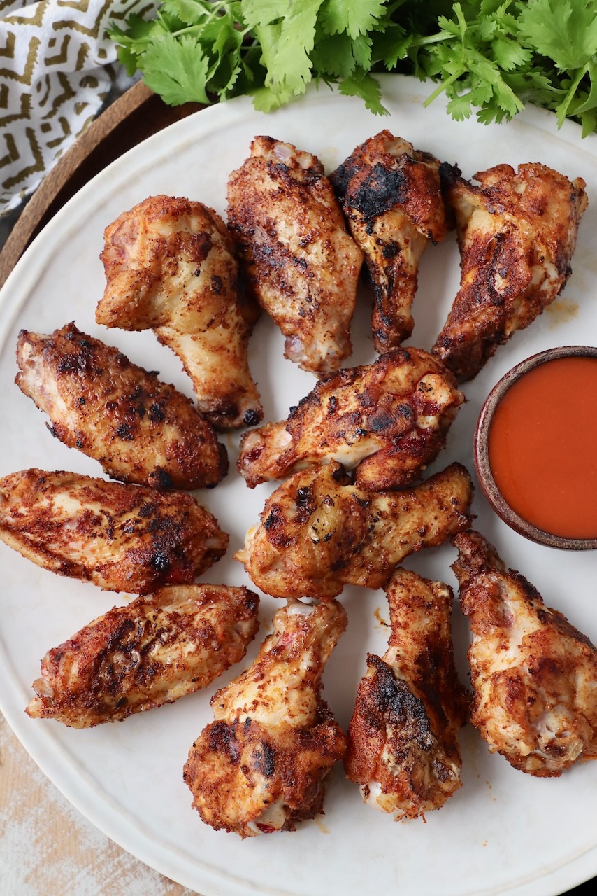 grilled chicken wings on plate with small bowl of buffalo sauce
