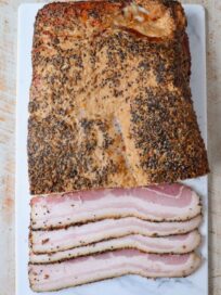 slab of homemade bacon on cutting board with slices of uncooked bacon