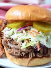 pulled pork sandwich topped with coleslaw and pickles on a plate