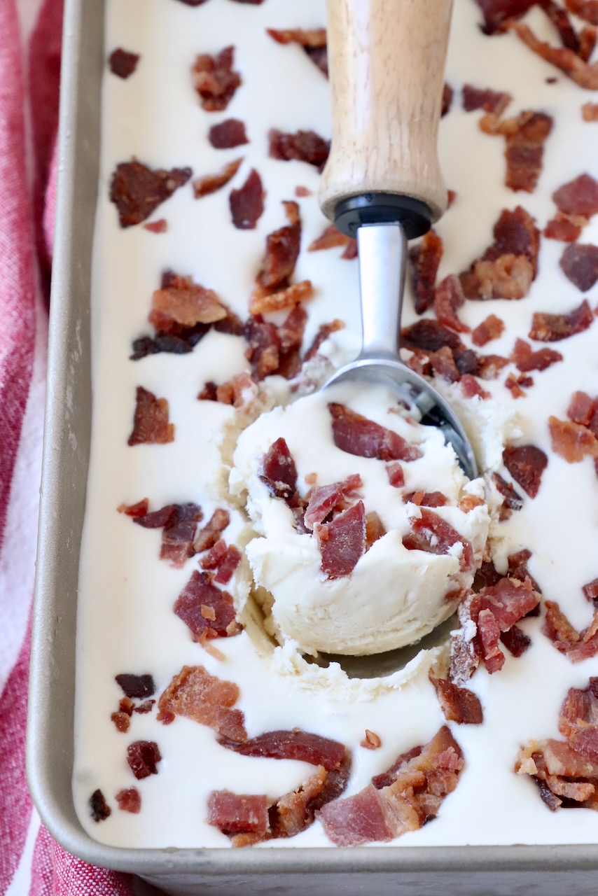 ice cream in metal container with ice cream scoop topped with candied bacon