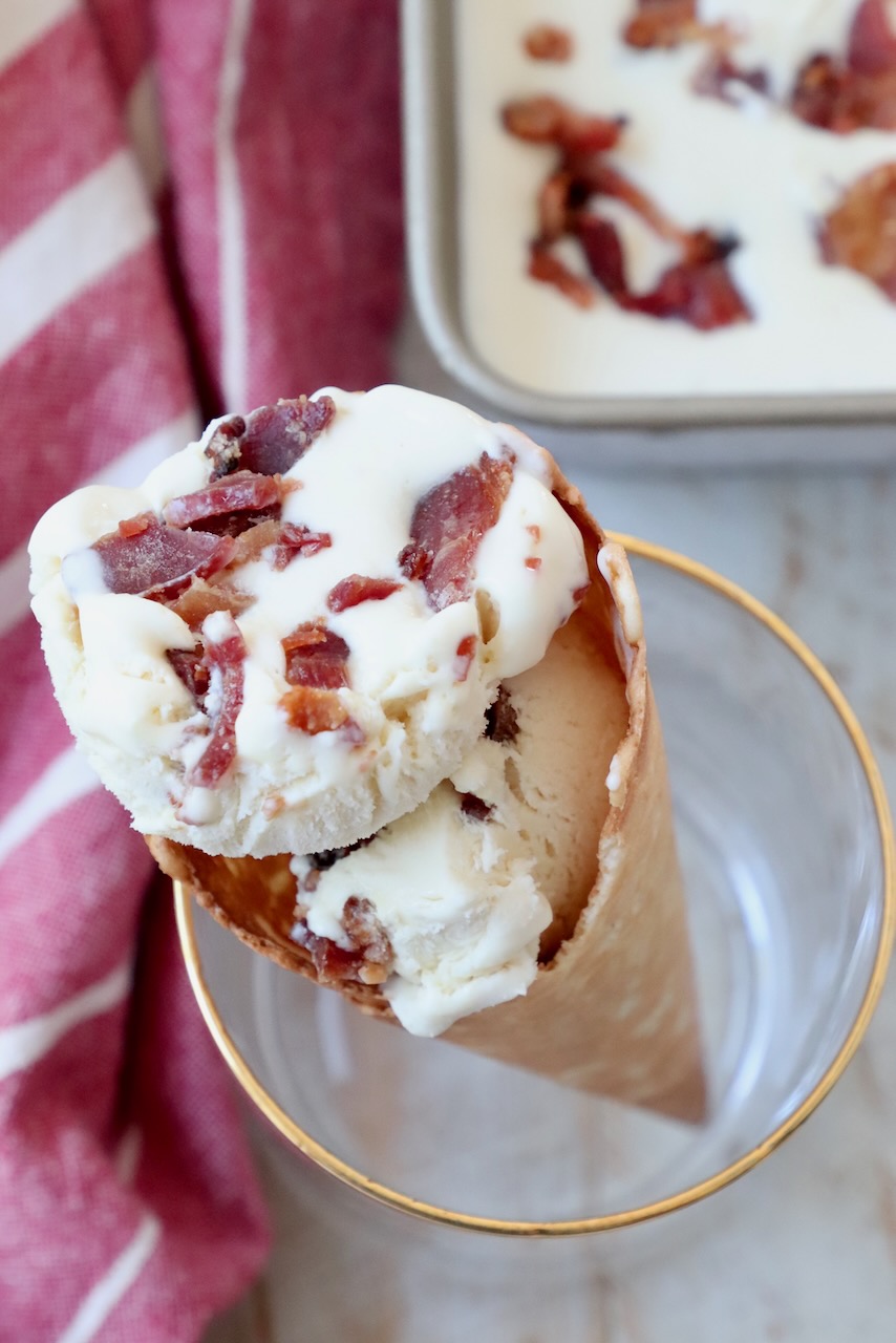 scoops of maple bacon ice cream in a waffle cone, held up in a drink glass