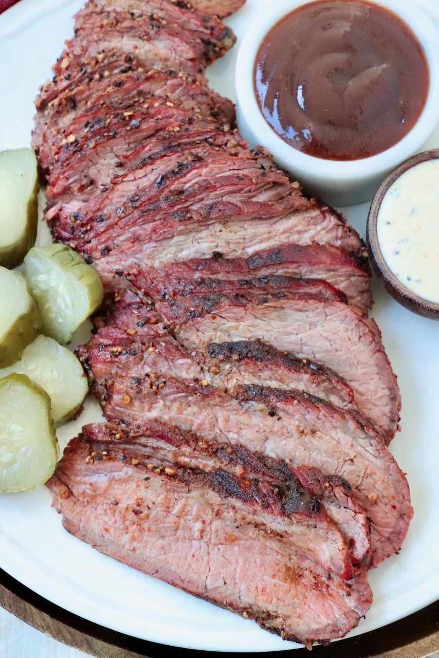 sliced smoked tri tip on plate with bbq sauce and sliced pickles