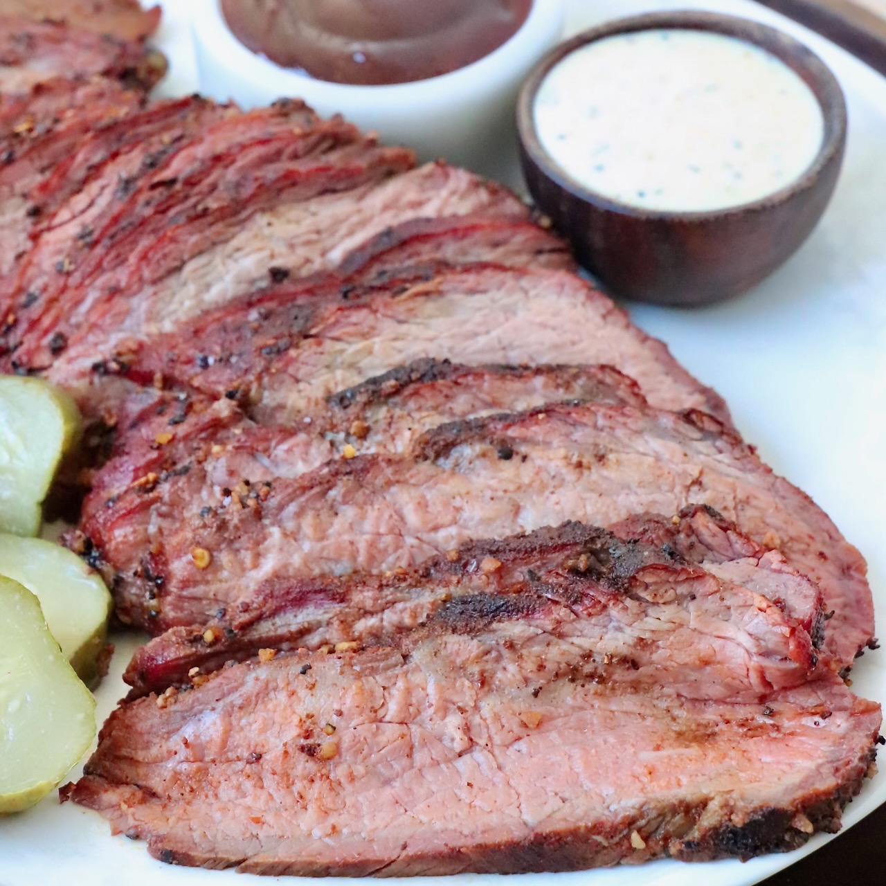 sliced smoked tri tip on plate with bowls of bbq sauce