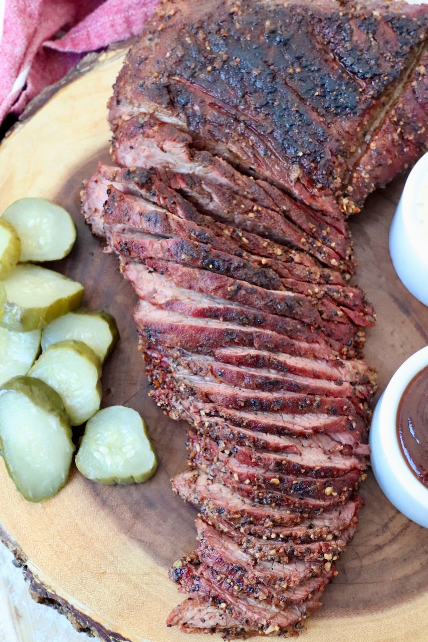 sliced smoked tri tip on cutting board with pickles
