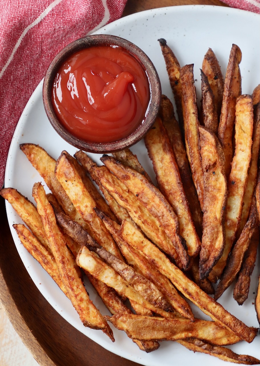 seasoned cooked french fries on plate with a small bowl of ketchup