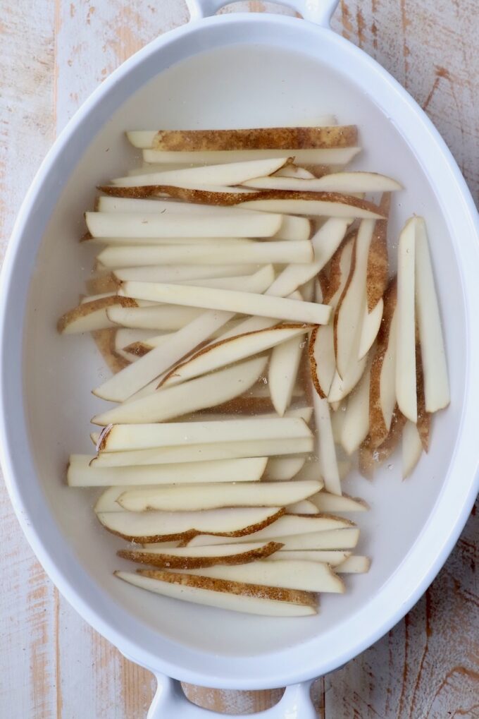 sliced potatoes soaking in casserole dish filled with water
