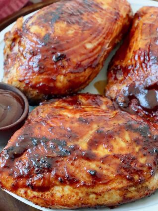 grilled bbq chicken breasts on plate with side bowl of bbq sauce