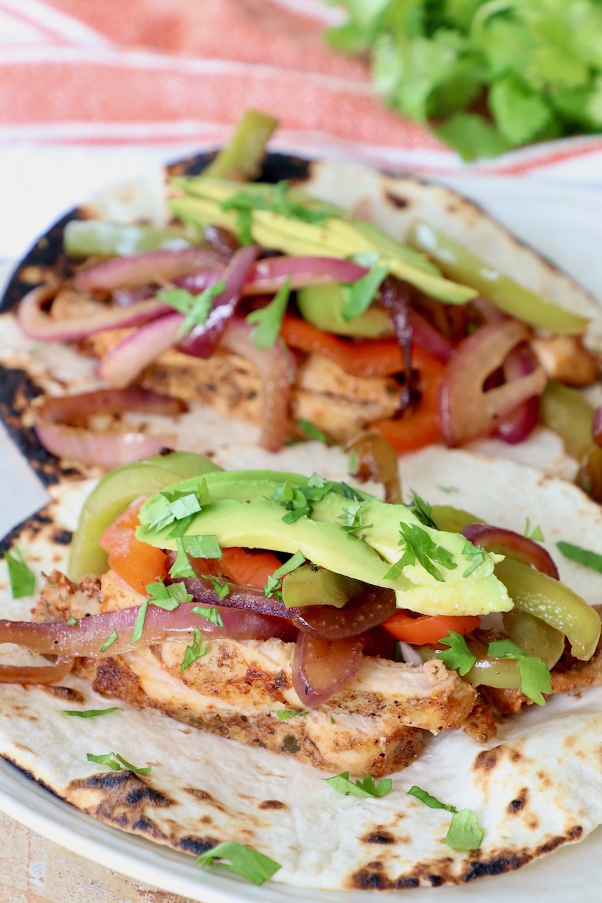 chicken fajitas on plate topped with sliced avocado and cilantro