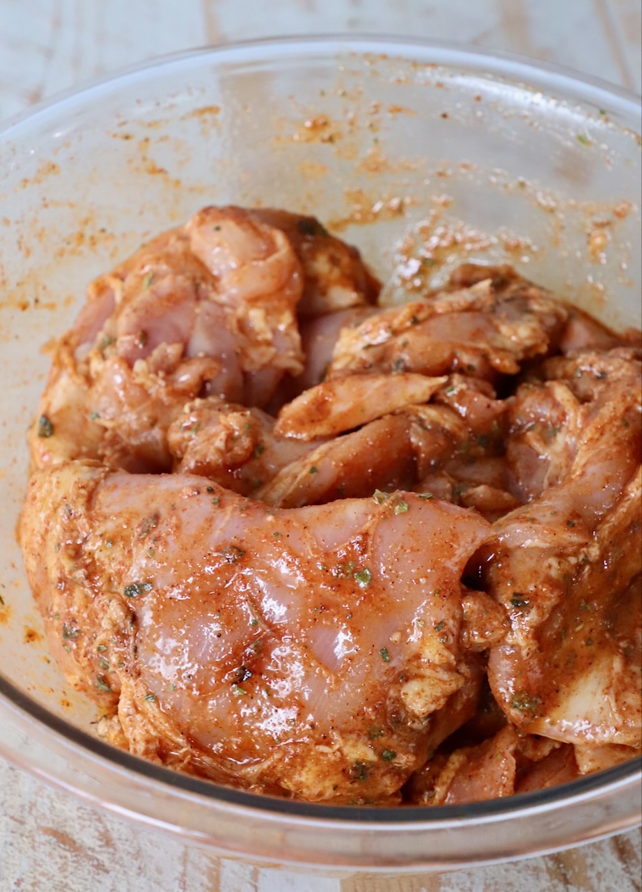 raw chicken thighs covered in marinade in large glass bowl
