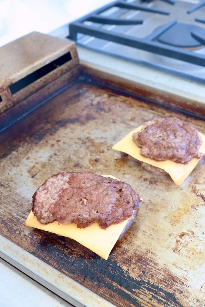 smashed burgers with slices of American cheese on griddle