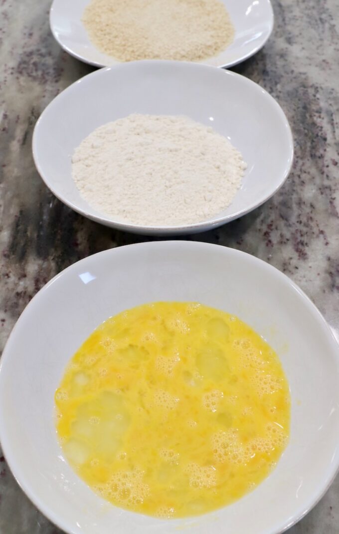 three bowls on countertop, one with whisked egg, one with flour and one with breadcrumbs
