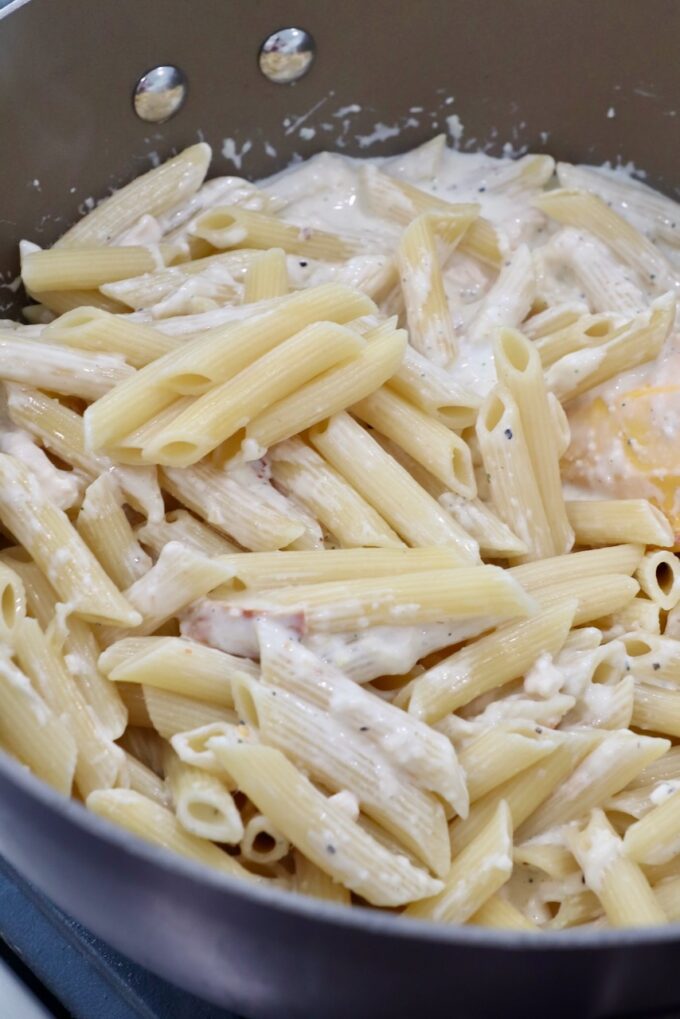 cooked pasta tossed with white sauce in pan