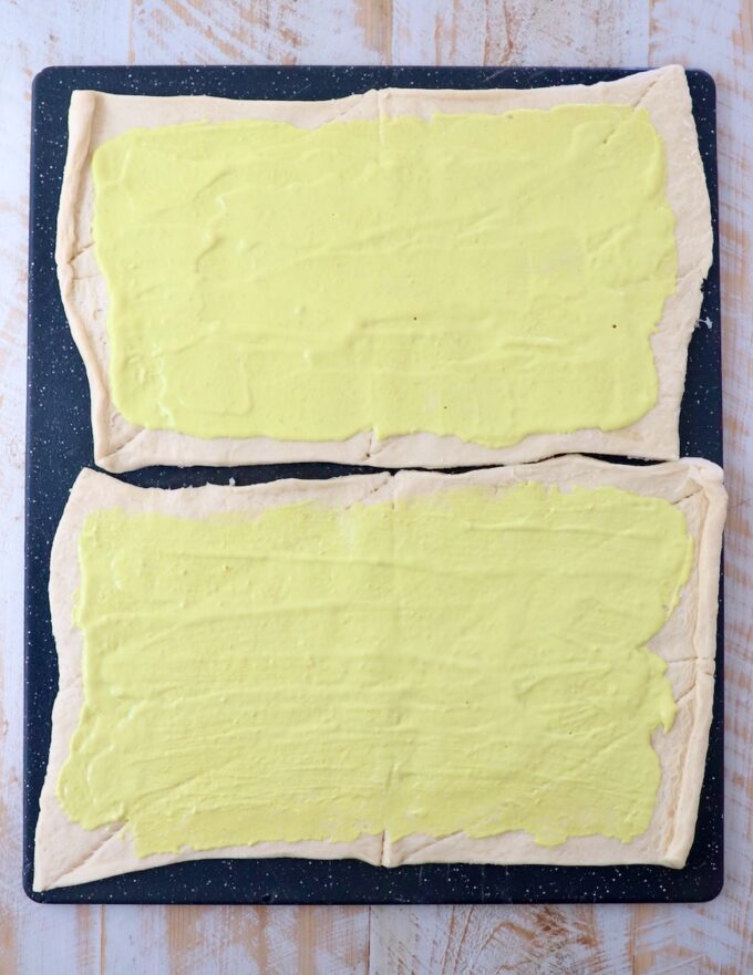 mayonnaise and mustard combined and spread on sheets of crescent roll dough on a large cutting board