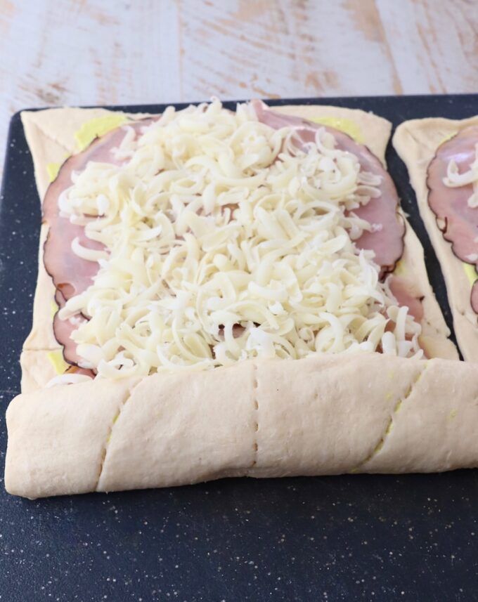crescent roll dough rolled up over ham and swiss cheese on a cutting board