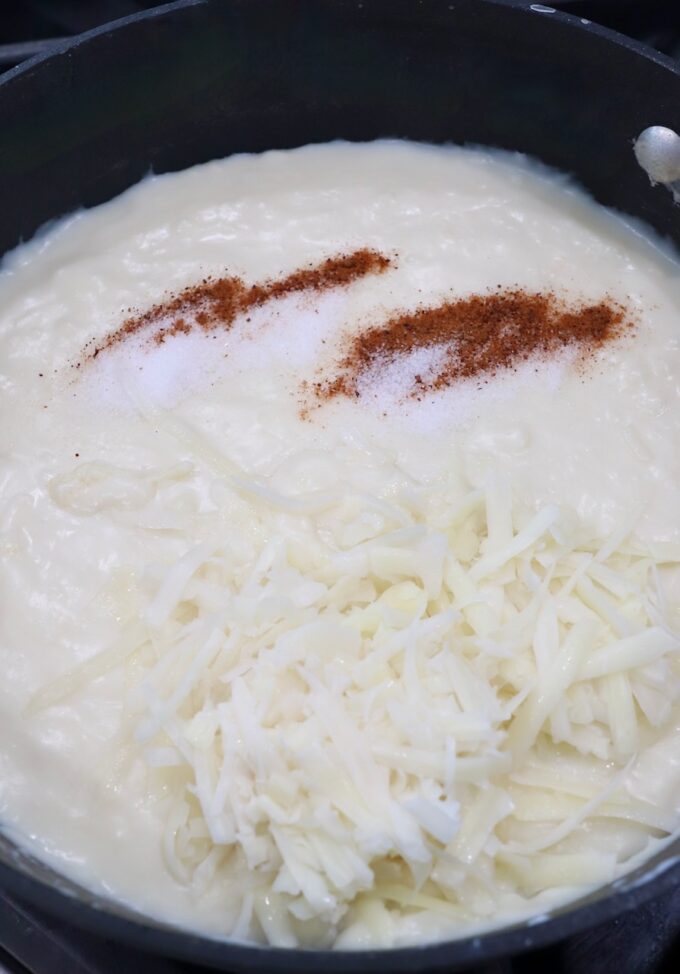 bechamel sauce in skillet with shredded cheese and spices
