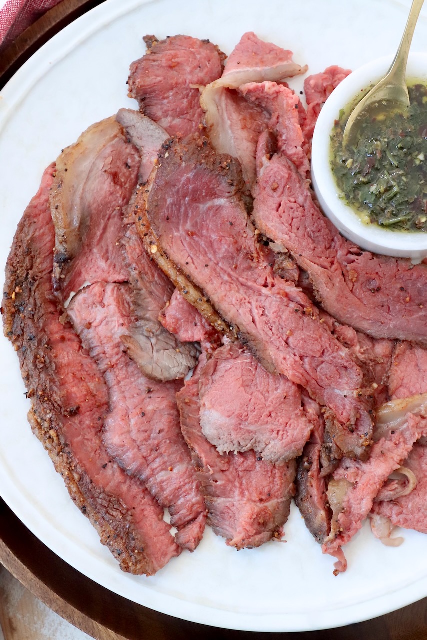 thinly sliced beef on large plate with a small bowl of herb butter sauce