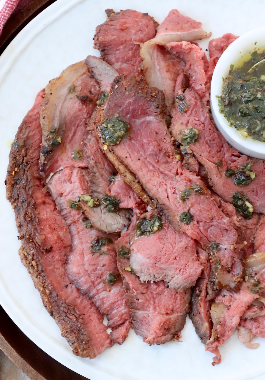 thinly sliced cooked steak on plate with herb sauce