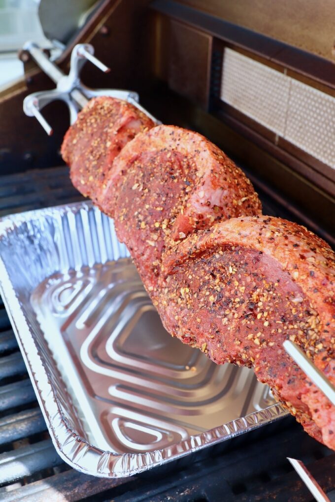 uncooked steaks on a rotisserie rod in a grill