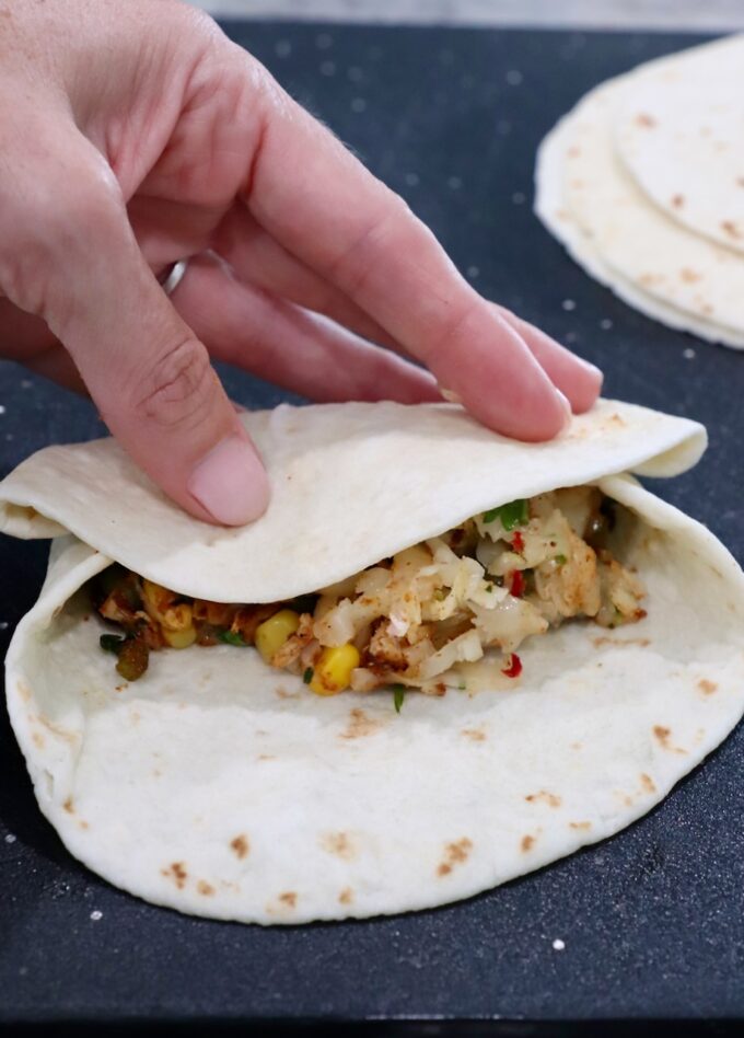 hand rolling tortilla over filling on cutting board