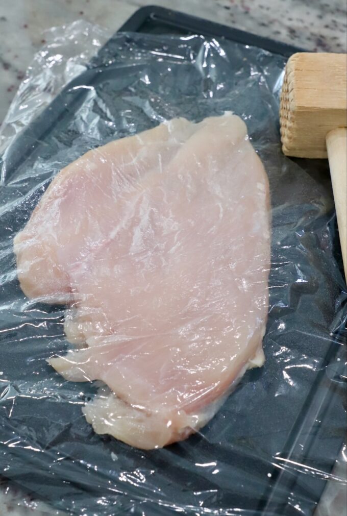 piece of chicken breast pounded thinly under plastic wrap on cutting board