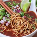 cooked ramen noodles lifted up with chopsticks in bowl of birria broth