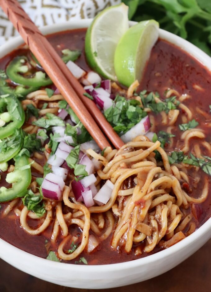 cooked ramen noodles in beef broth in bowl topped with diced onions and sliced jalapenos
