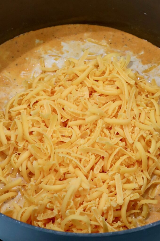 shredded cheddar cheese in seasoned cream sauce in large pan