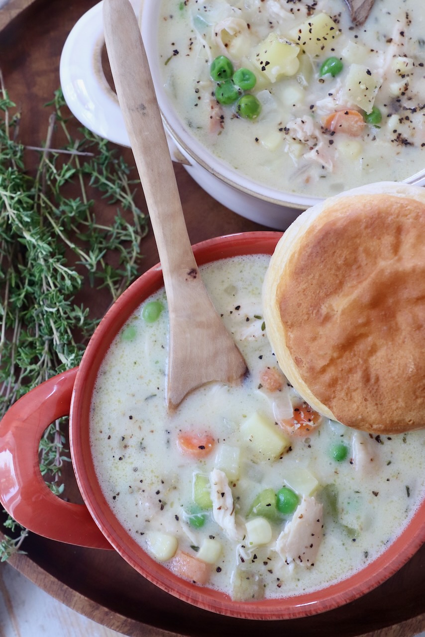 chicken pot pie soup in bowls with wooden spoon, topped with a biscuit
