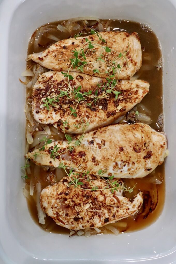 seared chicken breasts in slow cooker with fresh thyme sprigs and caramelized onions