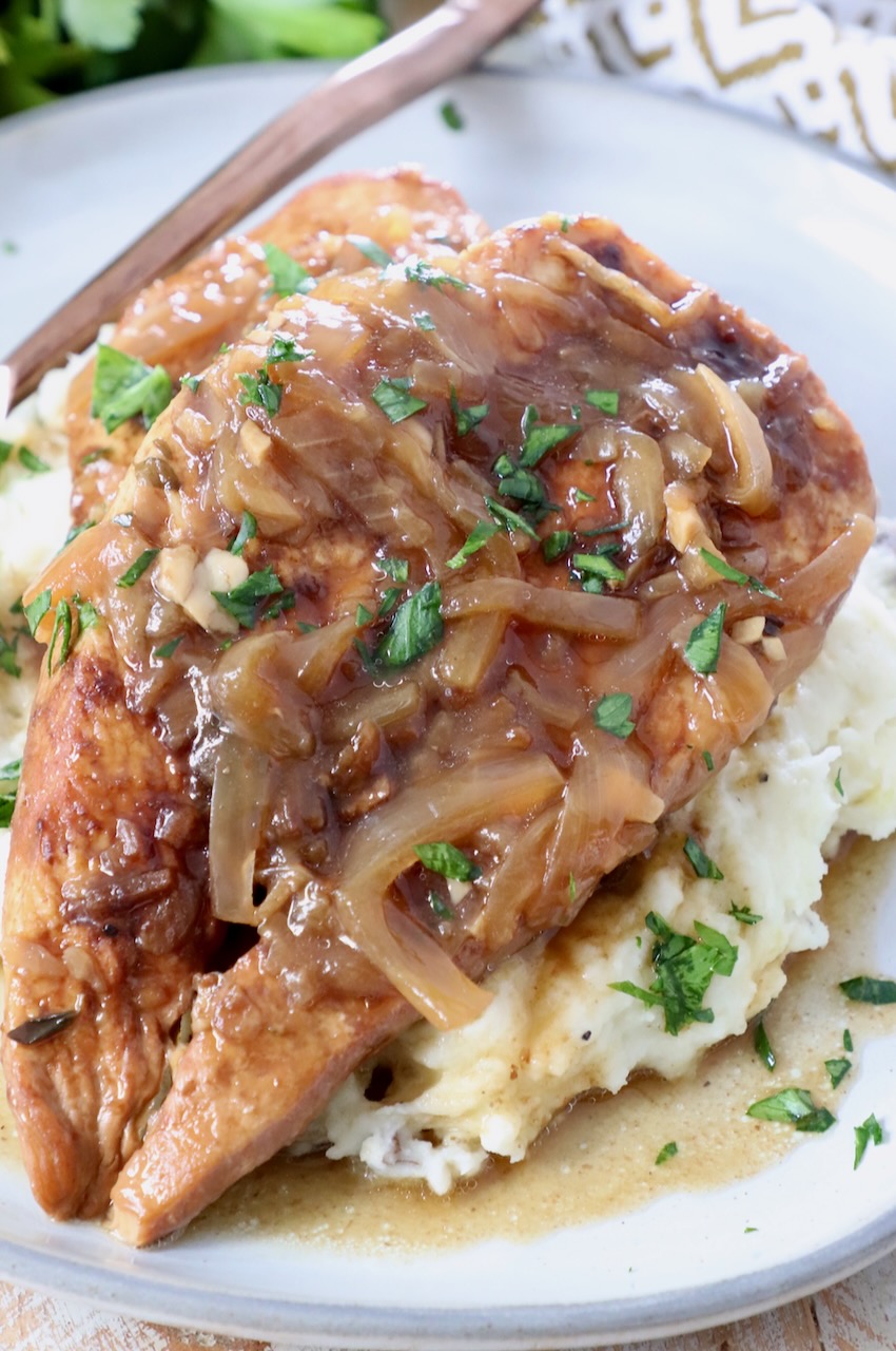 cooked chicken breasts with caramelized onion gravy on top of mashed potatoes on plate
