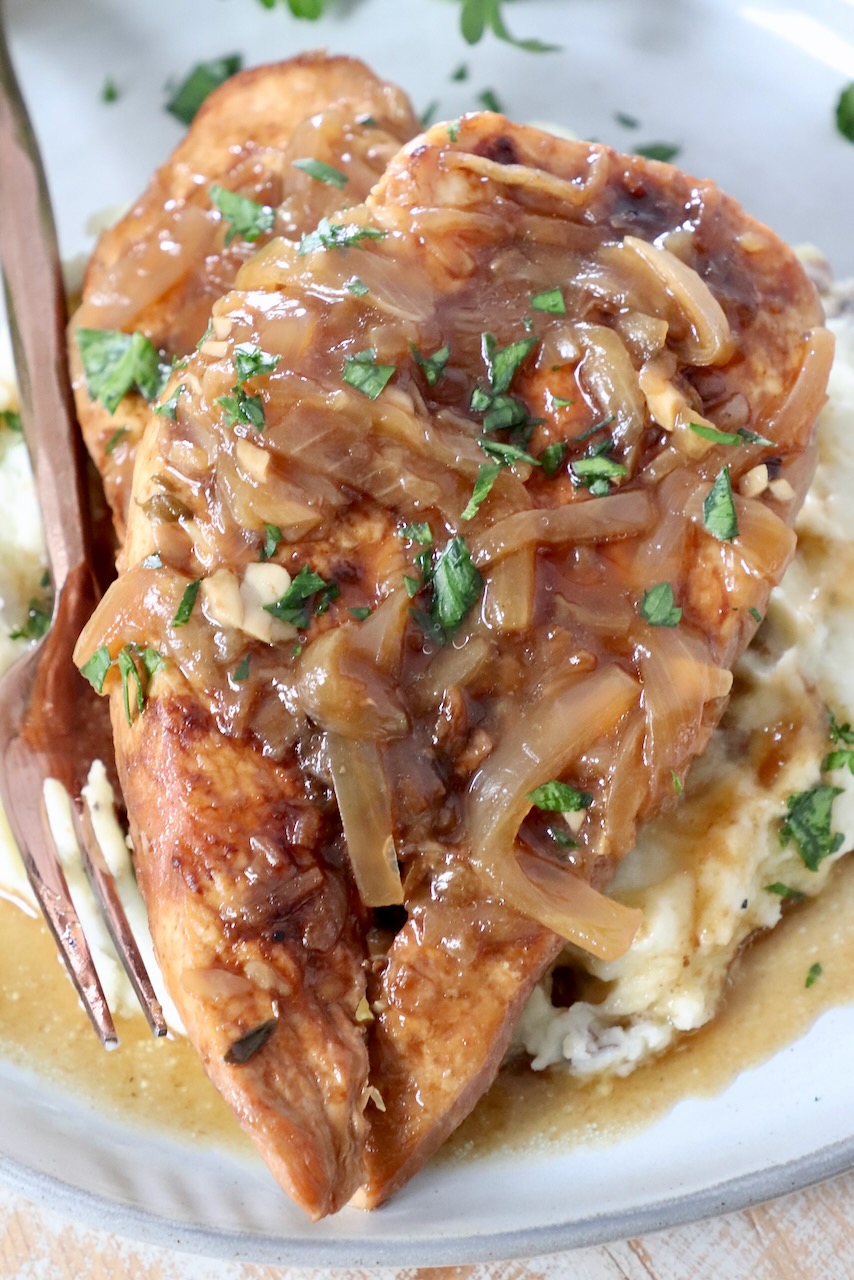 cooked chicken breasts on plate with caramelized onion gravy