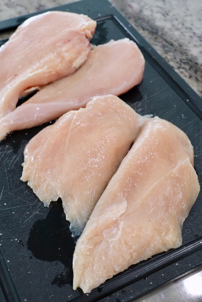 raw chicken breasts sliced in half on cutting board