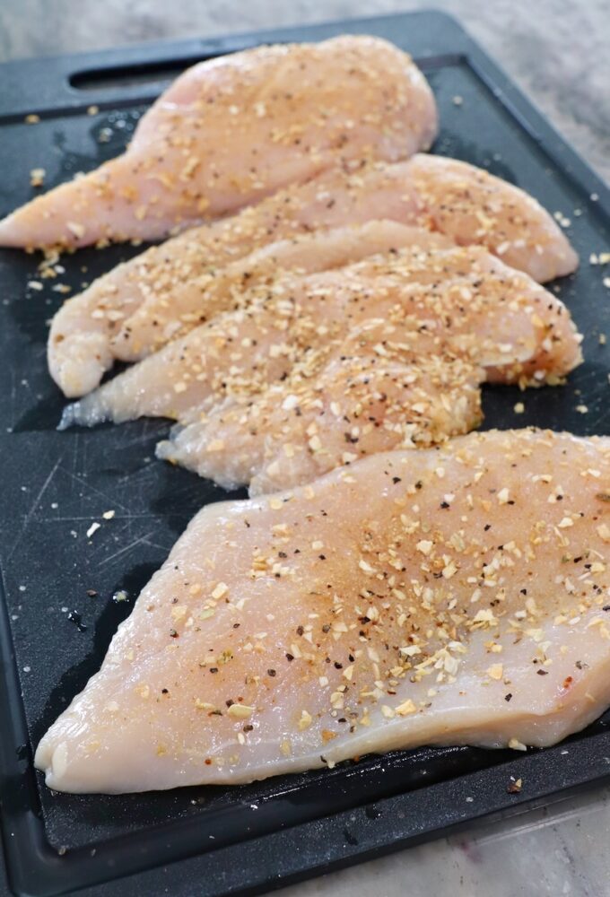 seasoned raw chicken breasts, sliced in half on cutting board