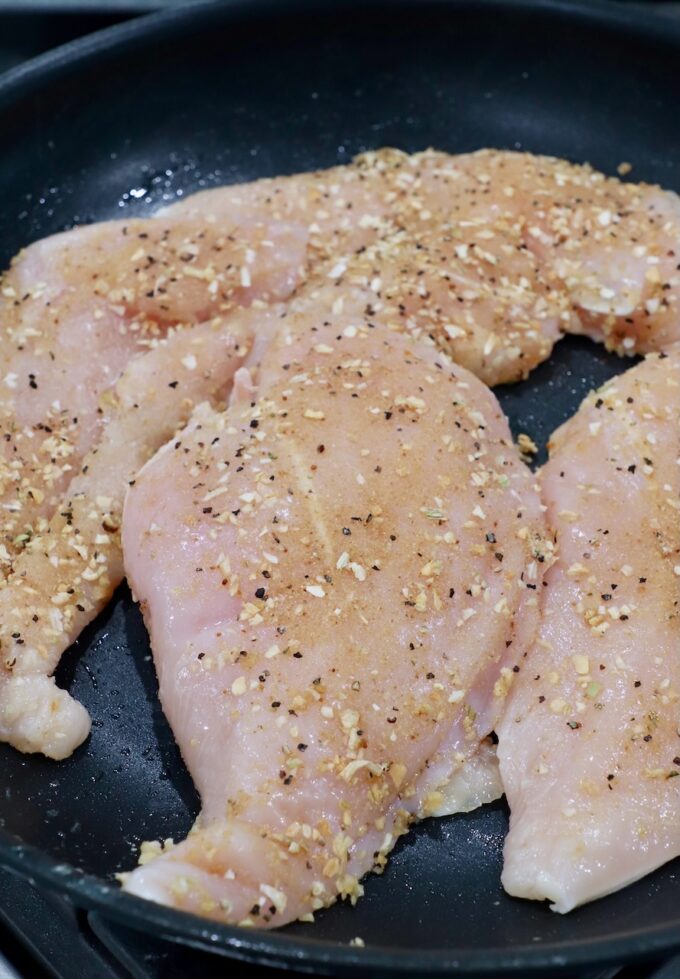 raw, seasoned chicken breasts in skillet