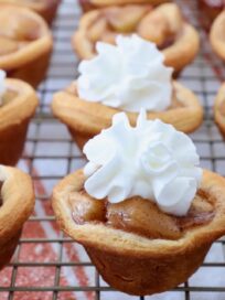 mini apple pies on wire rack topped with whipped cream