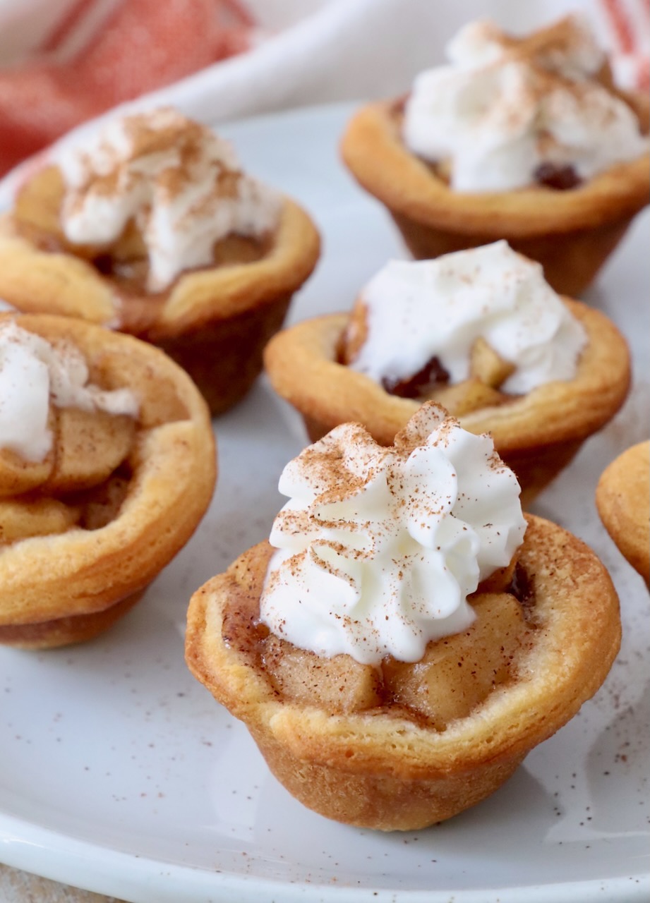 mini apple pies on plate, topped with whipped cream and ground cinnamon