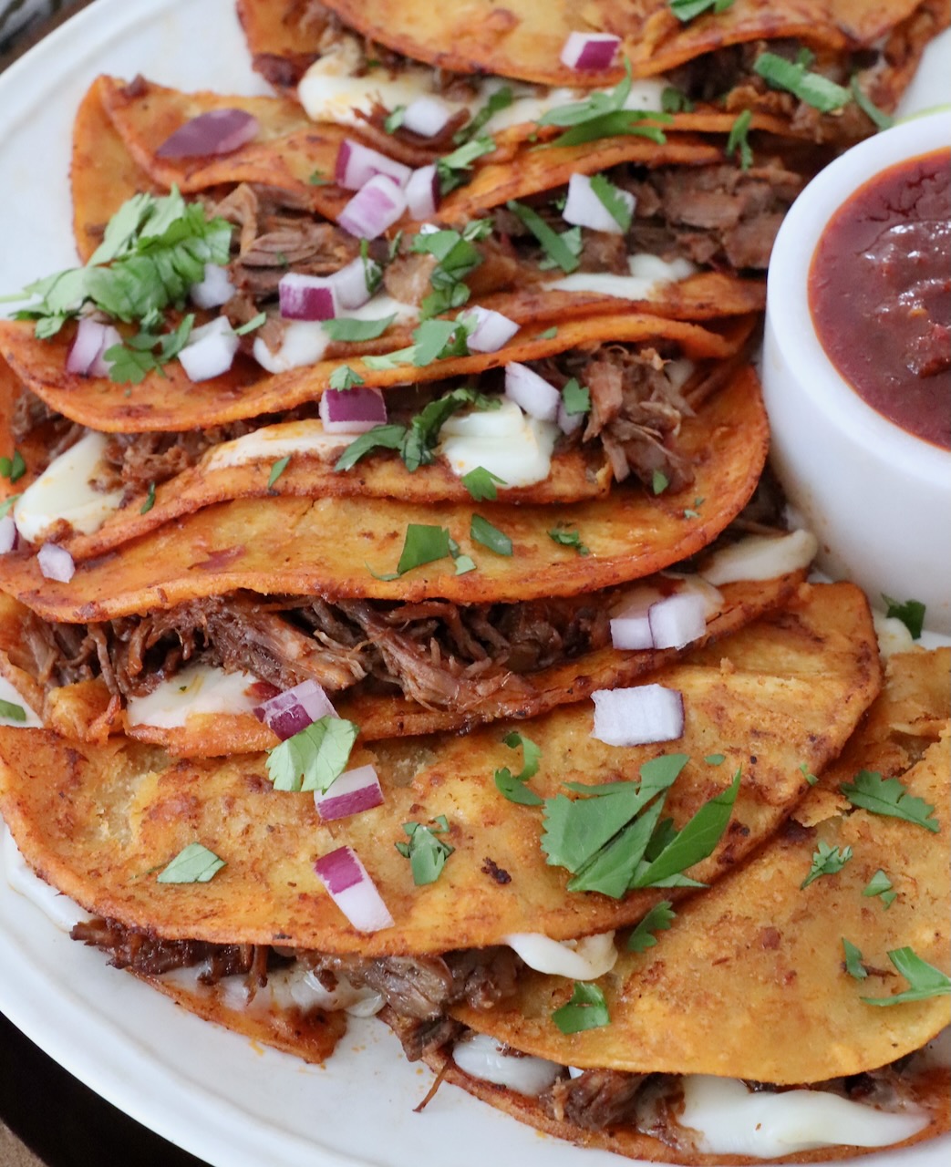 quesabirria tacos on plate with side of tomato beef broth in a small bowl