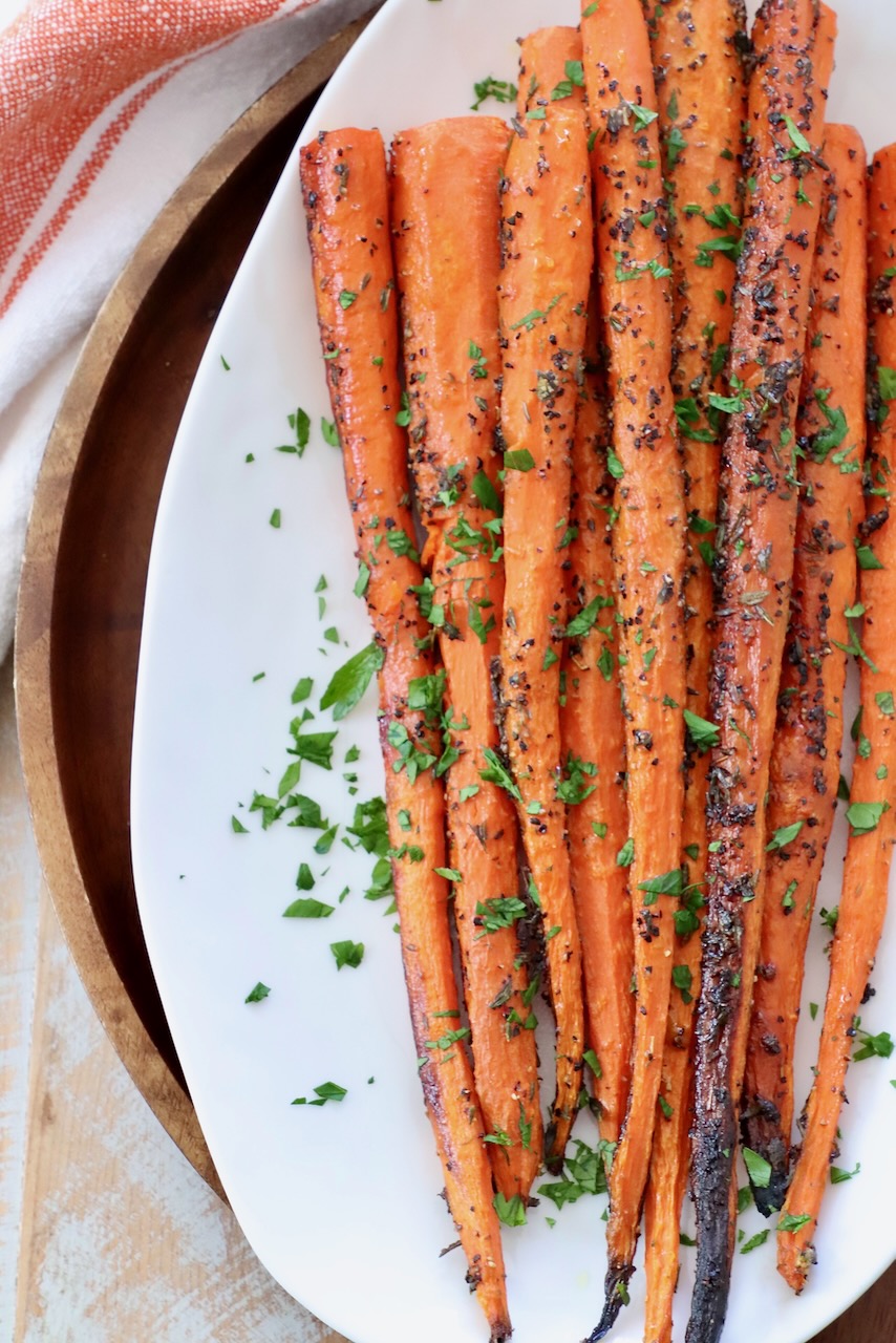 whole roasted carrots on white plate with fresh herbs 