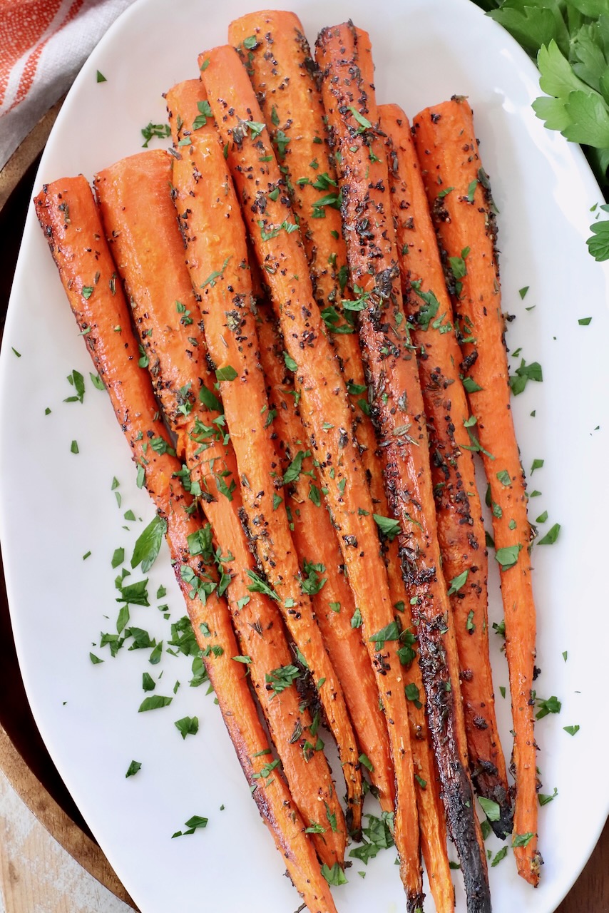 roasted carrots topped with fresh chopped parsley on white plate