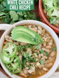 white chicken chili in bowls topped with sliced jalapenos and avocado